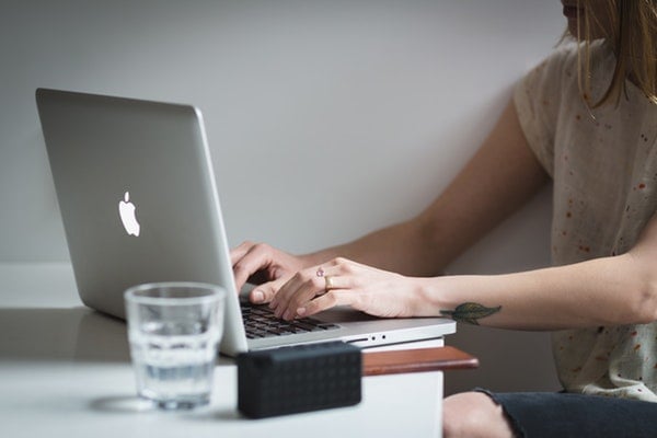 person at desk with apple laptop and glass of water