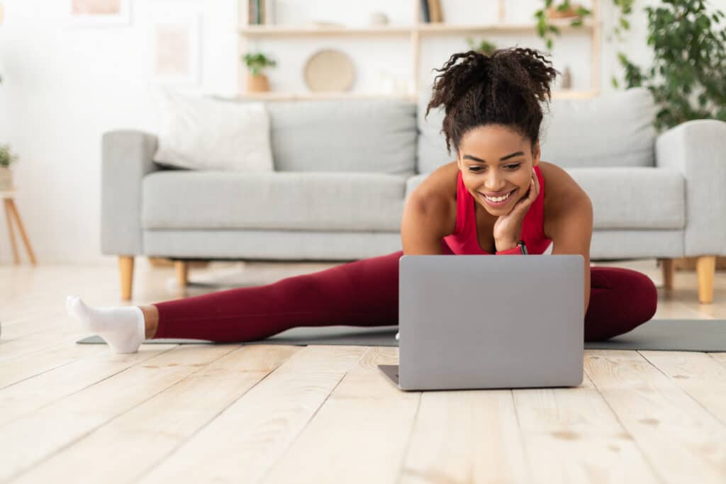 woman stretching legs on ground with laptop on floor