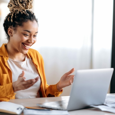 Woman holding hands up and smiling at a laptop