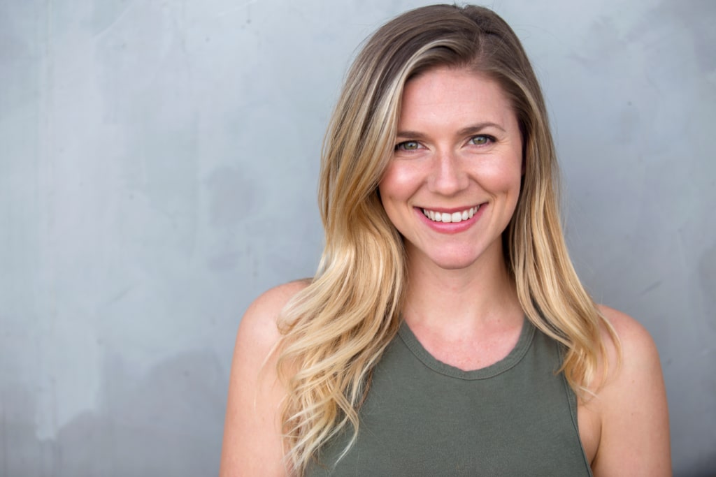 Headshot of blond woman in a green tank top in front of a grey background