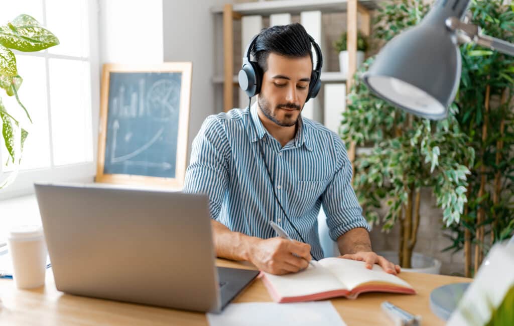 man with. headphones at a desk with a book and laptop computer