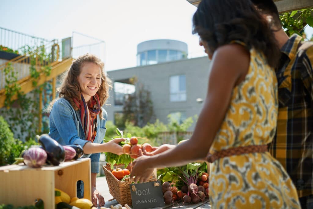 Female gardener selling organic crops and picking up a bountiful basket full of fresh produce