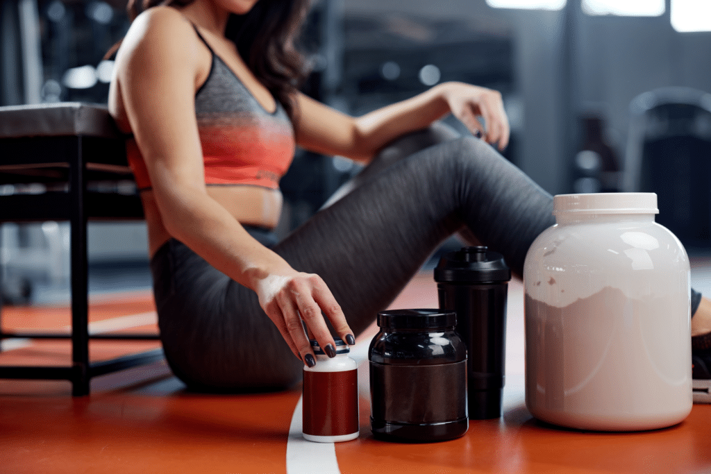 woman sitting on gym floor with supplement containers