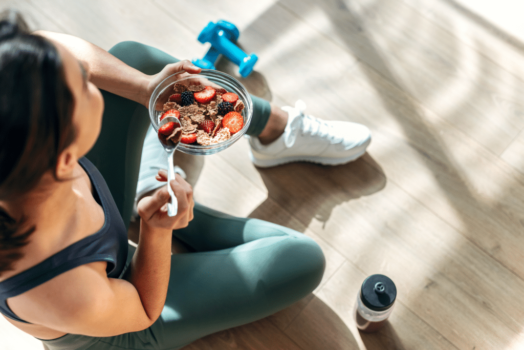 overhead shot of woman in workout clothes eating from a bowl with weights nearby