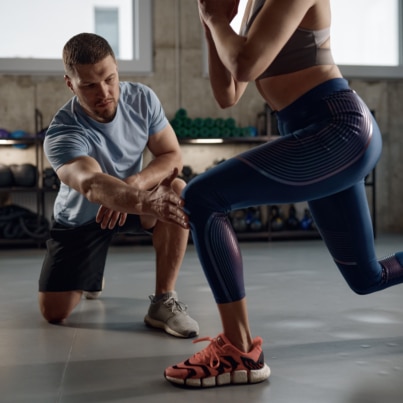 AFPA Certified Personal Trainer Coaching a Client in the Gym through a Lunge using the TRX