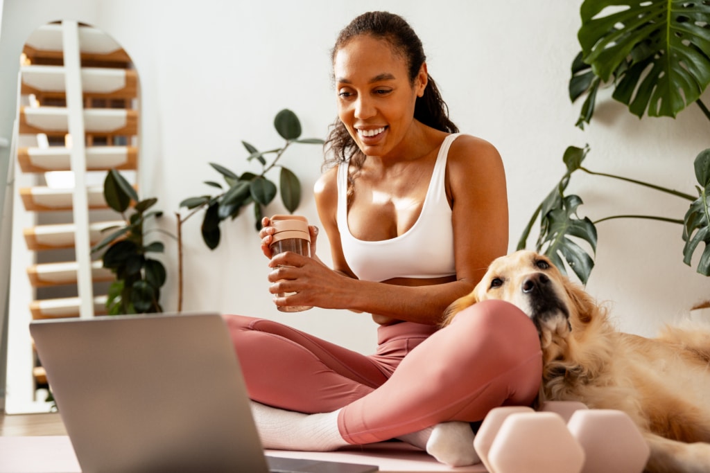 Woman in workout clothes sitting on floor with. laptop with golden retriever dog next to her